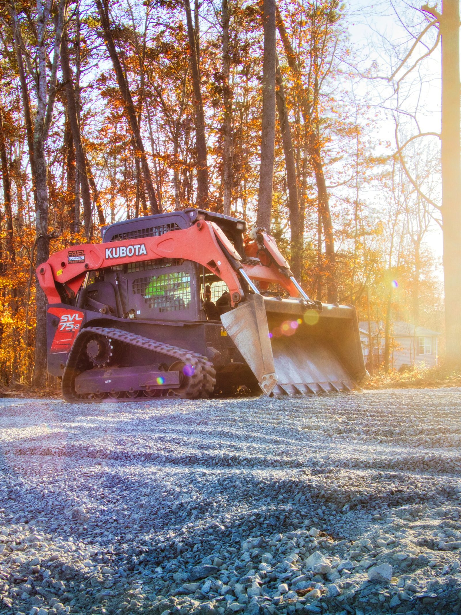Kubota SVL75-2 compact track loader grading gravel surface in wooded area, showcasing expert grading services for construction site preparation.