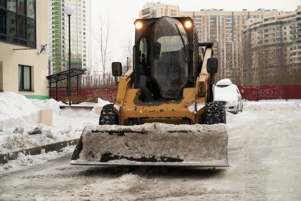 Skid steer loader clearing snow from a commercial property parking lot, emphasizing professional snow removal and ice management services.